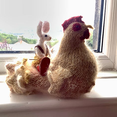 A knitted checking and a knitted rabbit become acquainted, the rabbit is sitting on the chicken and then the chicken is stood up.