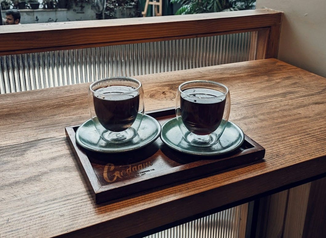 two cups of coffee sit on a tray in front of a window