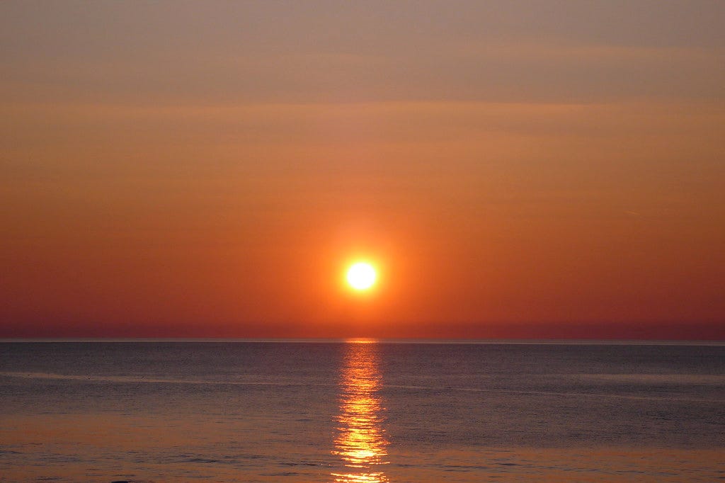 The sun going down behind the sea from in the sky. | Flickr