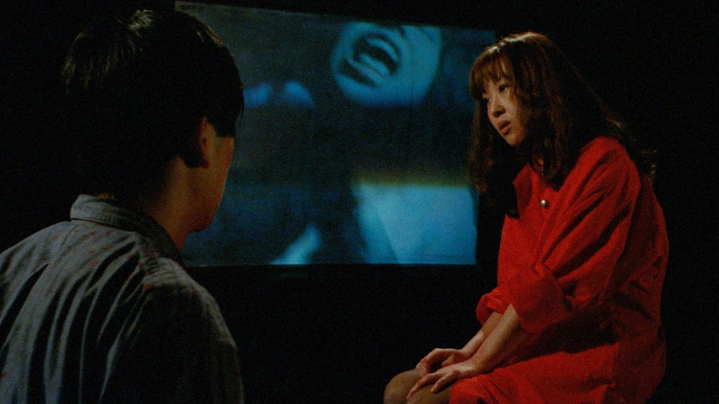 Re-Wind | Still features a dark room with two occupants, as a snuff film plays behind them.