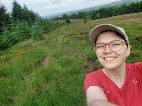 Smiling selfies of me mid walk. Behind me you see pink blooming Himalayan Balsam. In another picture is a straight grey road disappearing into the horizon. In another is a body of water, some grey clouds and lush grass in the foreground. Other pictures are of nature, a close up of an orange and black painted lady butterfly, dappled sun shining through woodland pines and a canal with reeds along its edge and algae on the water