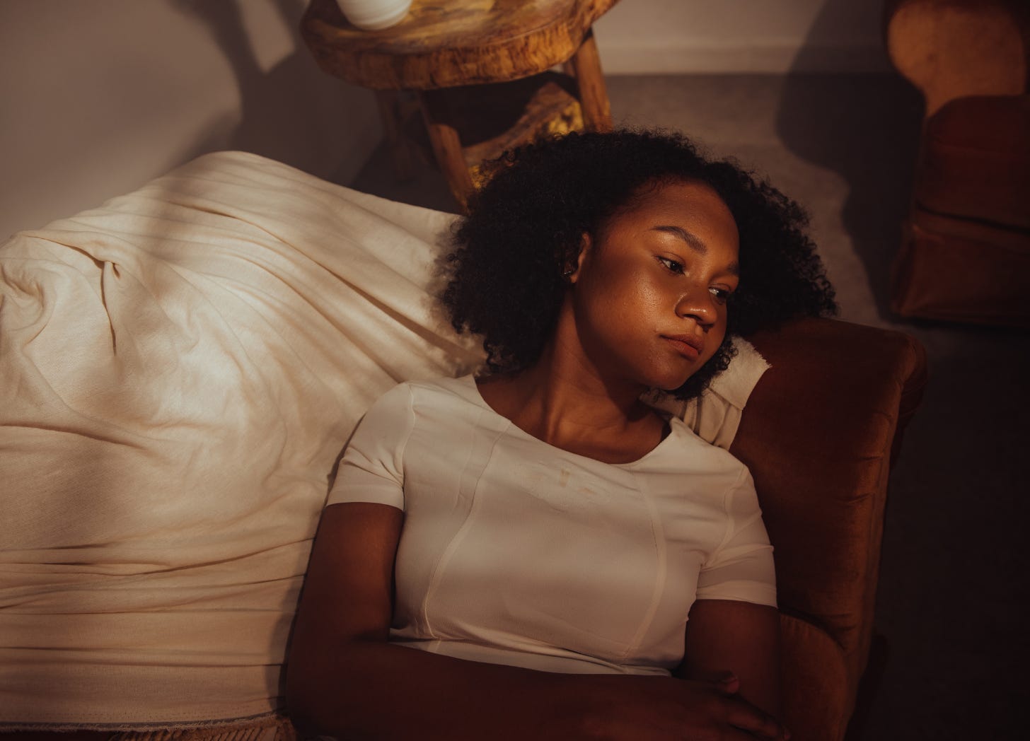 A young woman rests on a soft brown couch, bathed in warm, moody light. Her expression is quiet and introspective — like someone coming down from a long, emotional stretch, not in crisis but not quite settled either. A young woman rests on a soft brown couch, bathed in warm, moody light. Her expression is quiet and introspective — like someone coming down from a long, emotional stretch, not in crisis but not quite settled either.