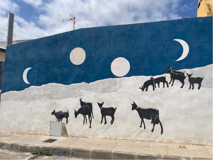 A photo of a mural depicting black goats on a hillside. Full and crescent moons rise above them.