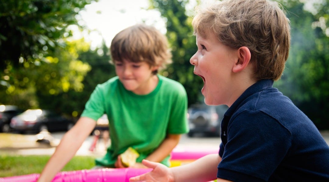 boy in blue shirt screaming near boy in green crew-neck shirt boy in blue shirt screaming near boy in green crew-neck shirt