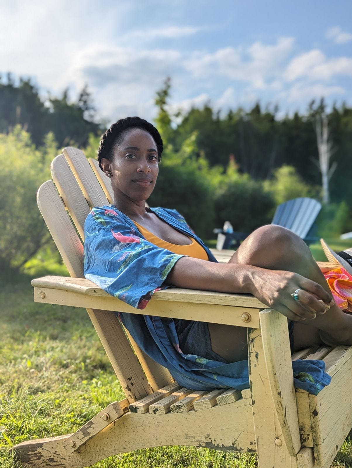 Image of Natalie seated outside in an Adirondack Chair wearing a yellow tank top and blue patterned shirt. Image of Natalie seated outside in an Adirondack Chair wearing a yellow tank top and blue patterned shirt.