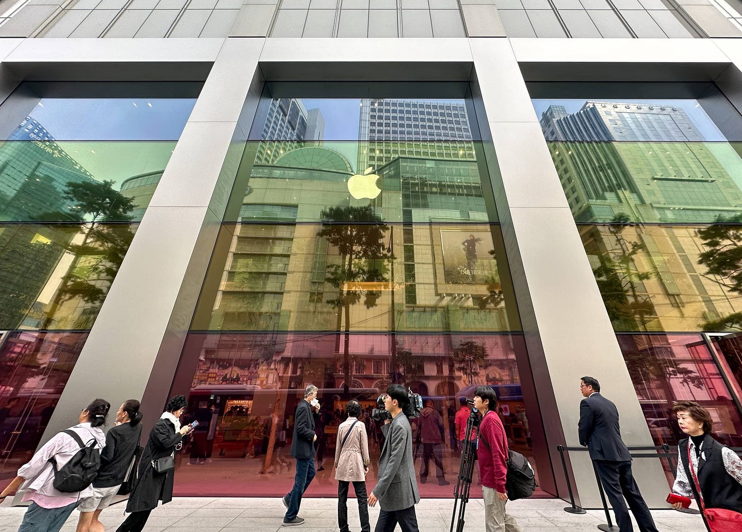 The facade of Apple Myeongdong. The windows are covered with horizontal bands of color matching the finishes of iPhone 15. The facade of Apple Myeongdong. The windows are covered with horizontal bands of color matching the finishes of iPhone 15.