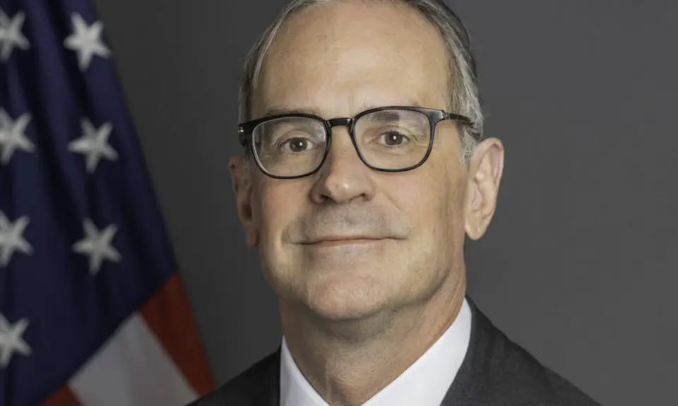 Formal portrait photo of Michael Anton in suit and tie looking into the camera with an American flag behind his right shoulder Formal portrait photo of Michael Anton in suit and tie looking into the camera with an American flag behind his right shoulder