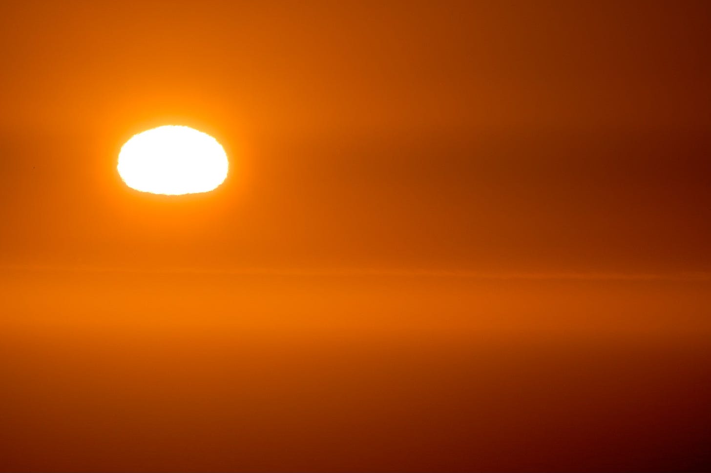 Orange sunset on the Oregon coast with the bottom of the son getting flattened 