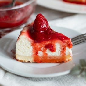 Photo of a slice of white cheesecake topped with strawberries, on a white plate, by Diliara Garifullina from Unsplash