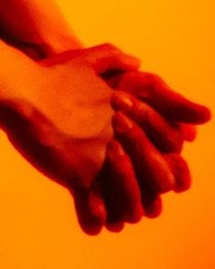 This may contain: two hands holding each other over an orange background