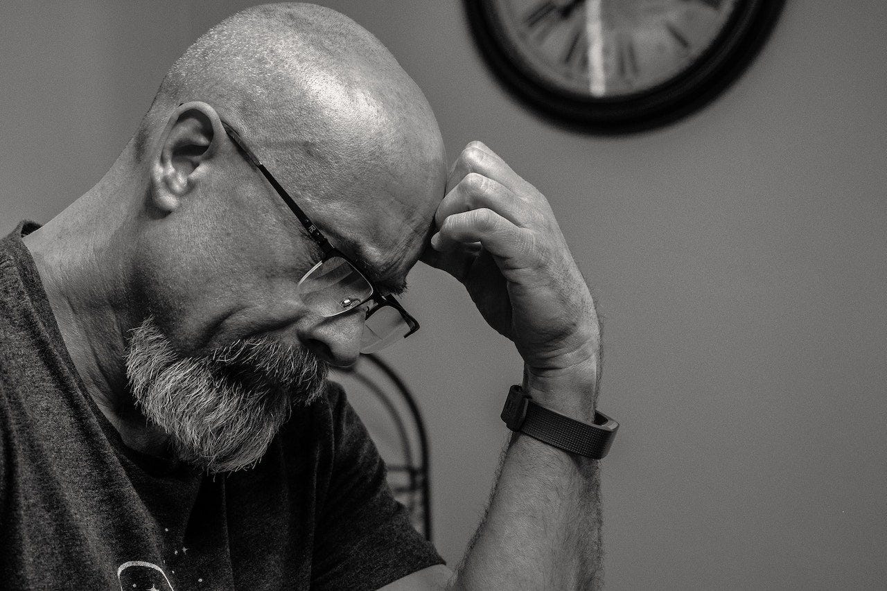 bald headed man with hand on head staring intently at the thing in front of him