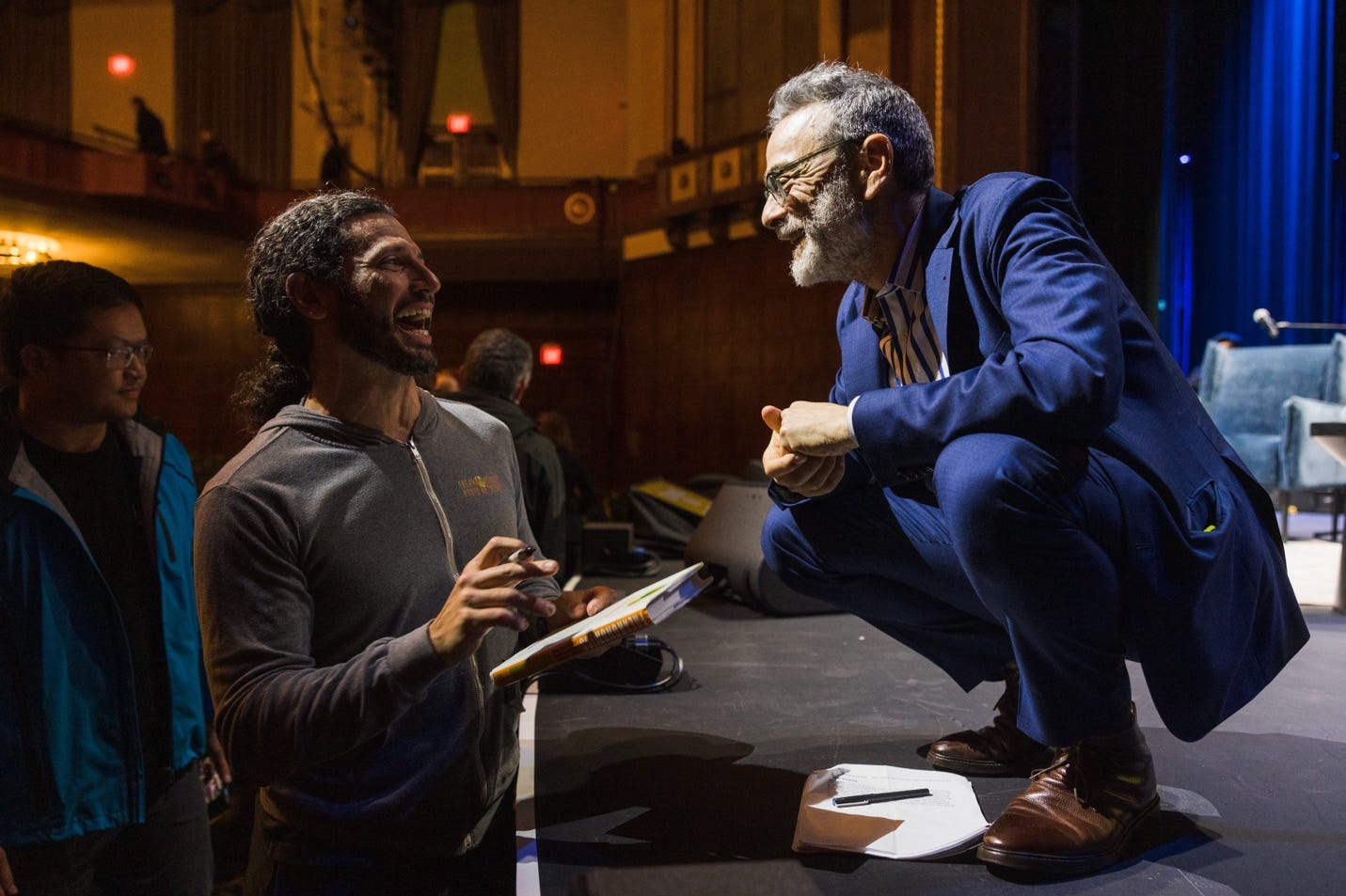 A person kneeling down and laughing while another person is holding a clipboard

Description automatically generated