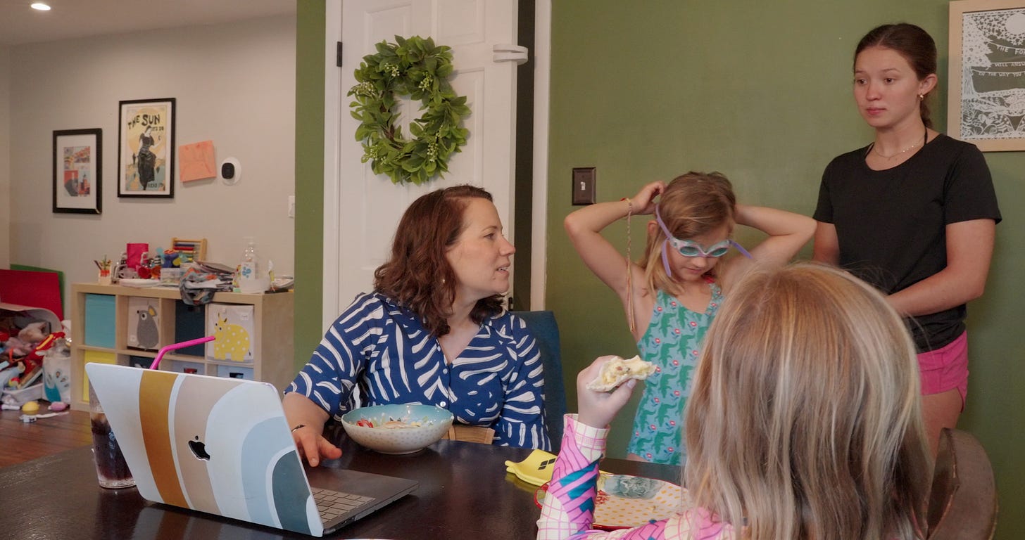 reporter sits at table with laptop open while talking to her kids and babysitter