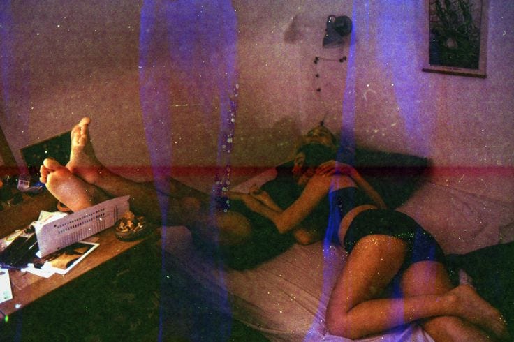 This may contain: two people laying on a bed in a room with purple light coming through the window