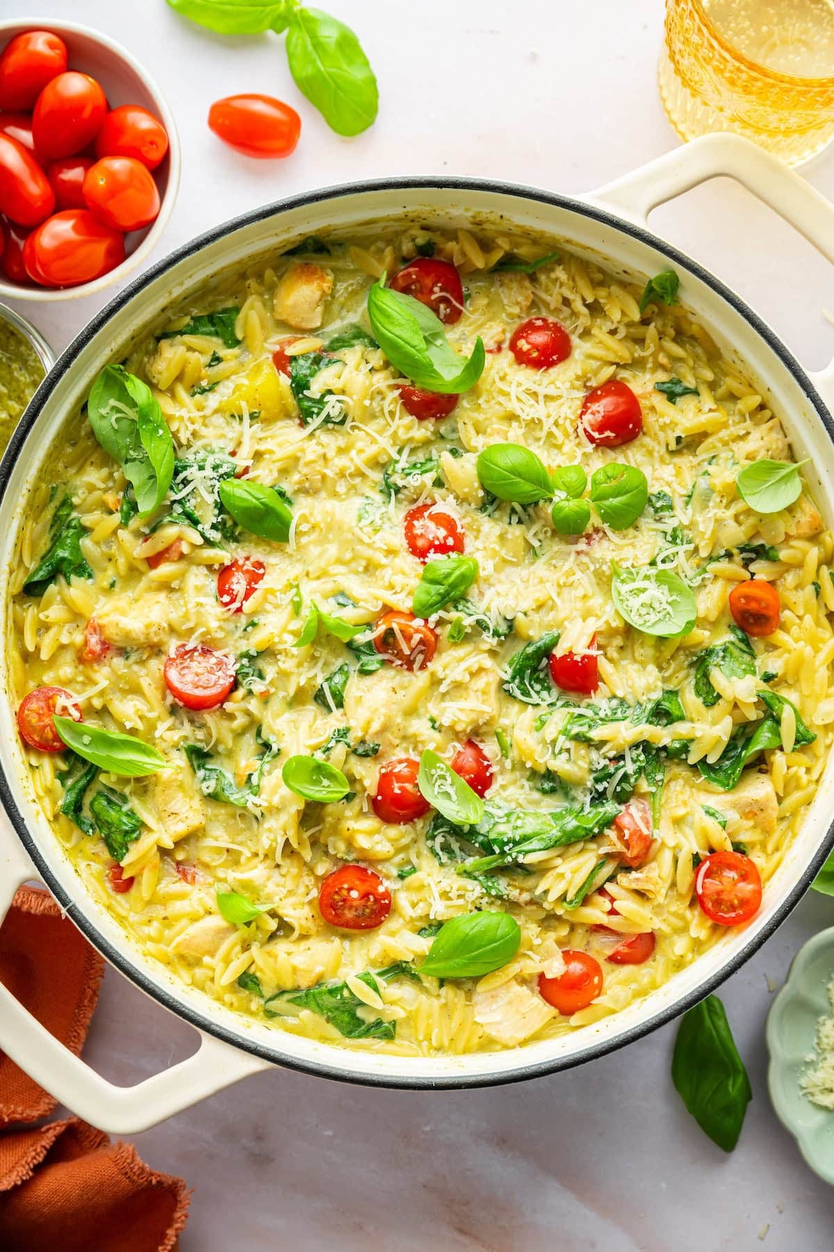 A large pot of pesto chicken, orzo, cherry tomatoes, spinach, parmesan cheese, and fresh basil.
