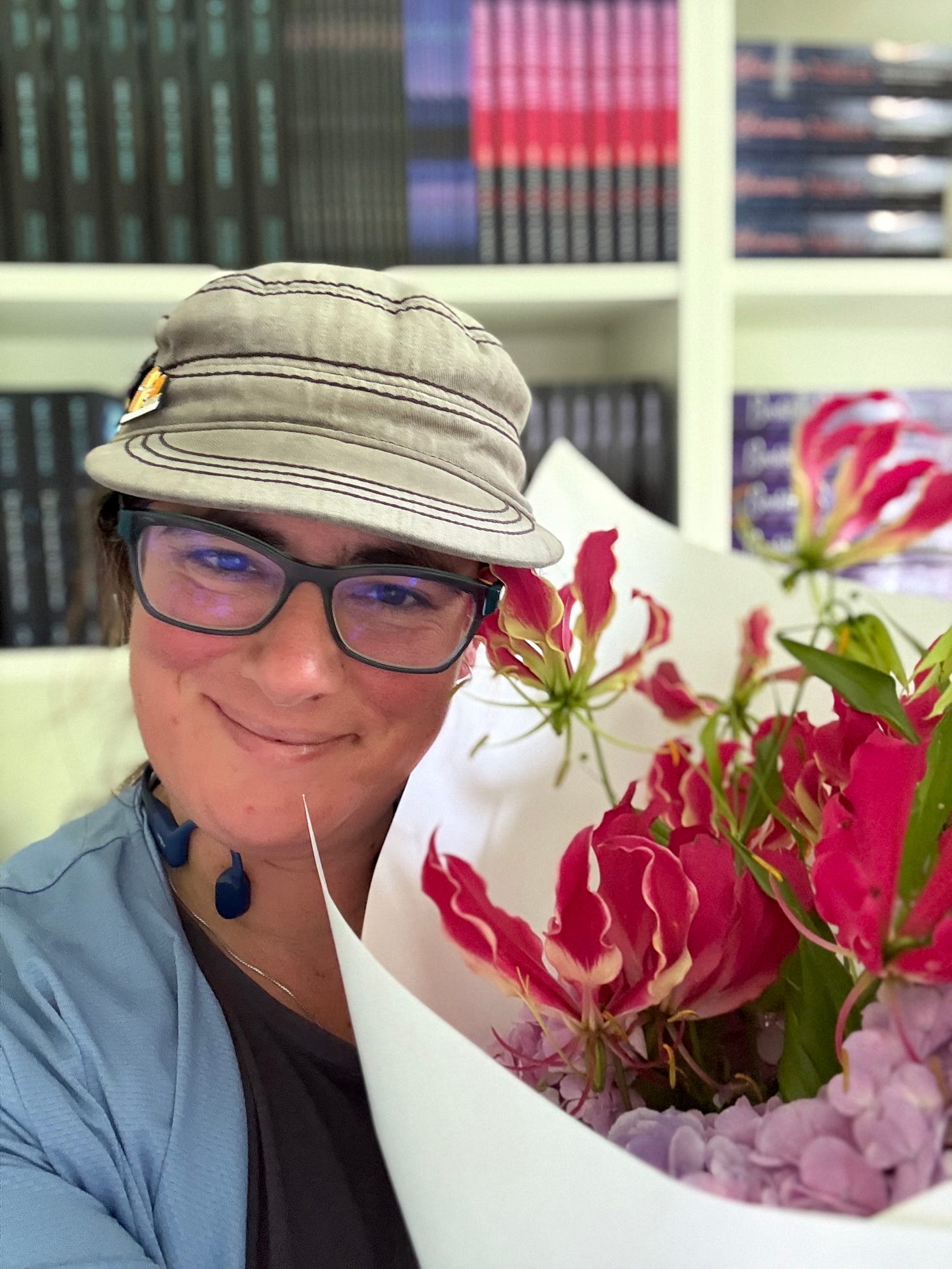 Author Miri Stone standing in front of her book stock, holding a boquet of flowers