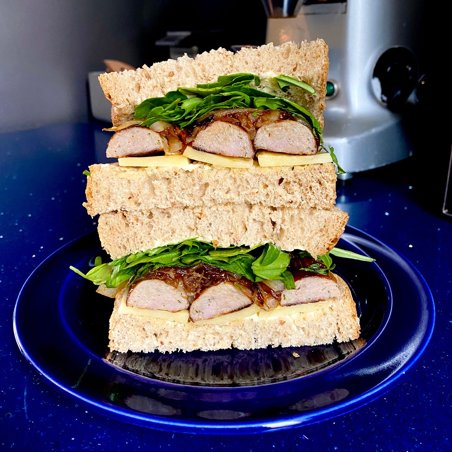 Cross section of a sausage sandwich showing bread, sausages, cheese, caramelised onions, and salad