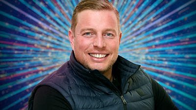 A head and shoulders shot of Thomas Skinner in a dark body warmer over a dark top, smiling to camera. He's set against a glittering blue background.