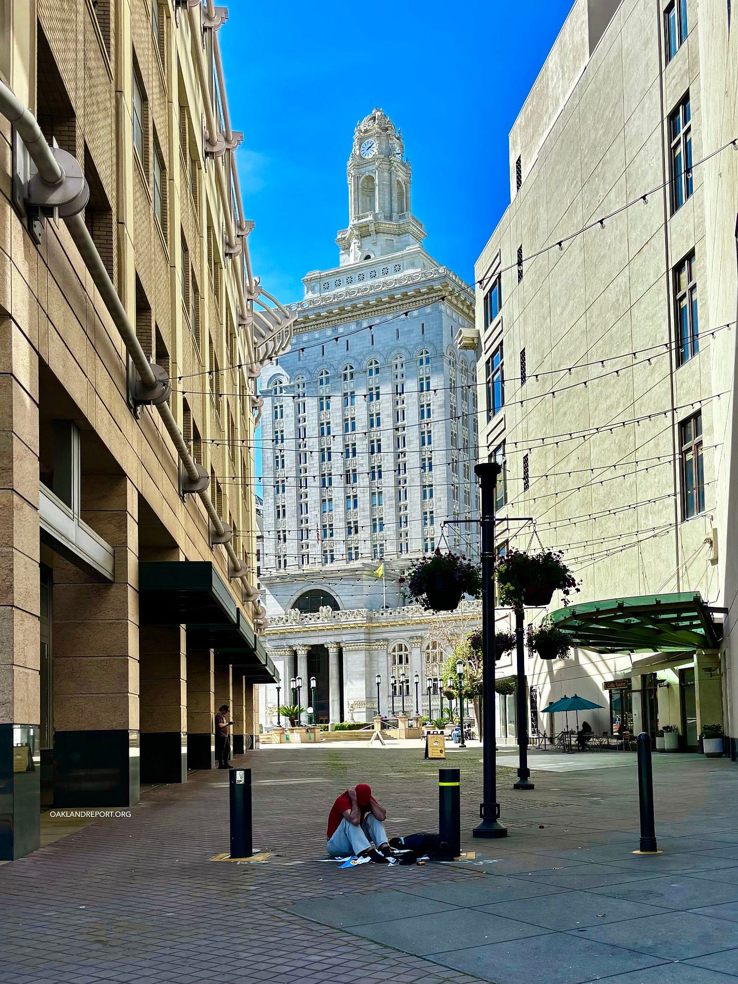 The data suggests that the roughly 1,075 people who vanished from Oakland’s count between 2024 and 2026 did not all move into shelters, because there were not enough for them to move into. (Image: A man sits on the pavement outside Oakland City Hall on Mar. 16, 2026 / Oakland Report) The data suggests that the roughly 1,075 people who vanished from Oakland’s count between 2024 and 2026 did not all move into shelters, because there were not enough for them to move into. (Image: A man sits on the pavement outside Oakland City Hall on Mar. 16, 2026 / Oakland Report)