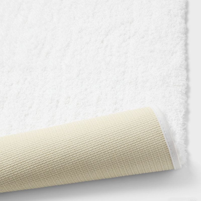 A white colored rug with a textured beige colored underside partially rolled up.