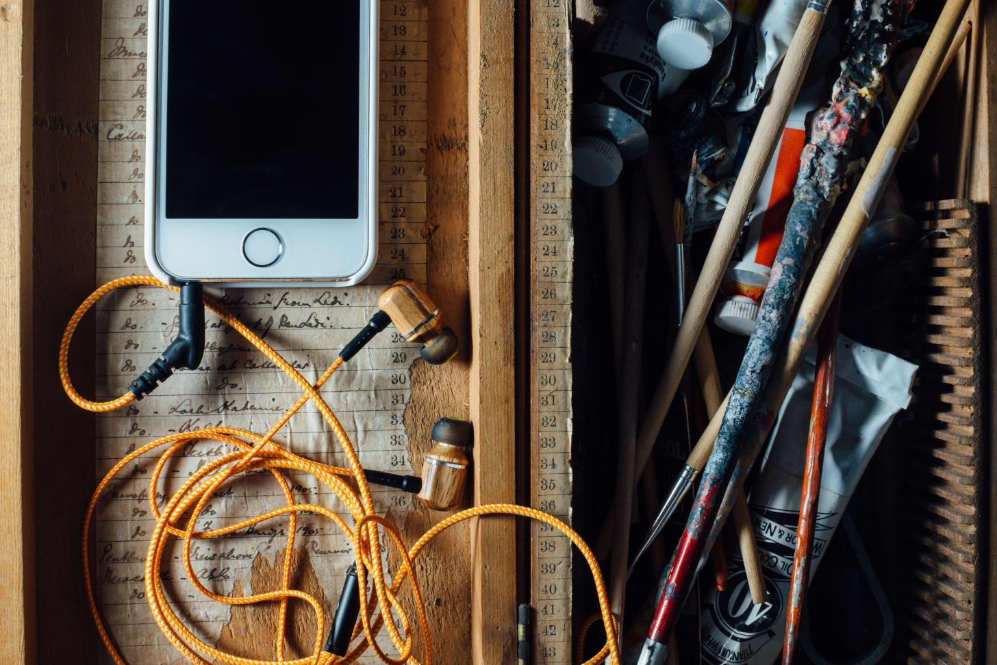 wood box with paints and brushes on one side and a smartphone with earbuds on the other wood box with paints and brushes on one side and a smartphone with earbuds on the other
