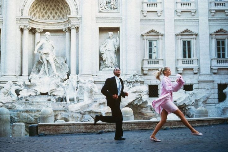 This may contain: a man and woman are running in front of a building with statues on the sides