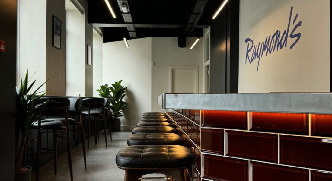 A brick bar area with a row of leather stools in front of it, with white walls around it and a black ceiling above it A brick bar area with a row of leather stools in front of it, with white walls around it and a black ceiling above it