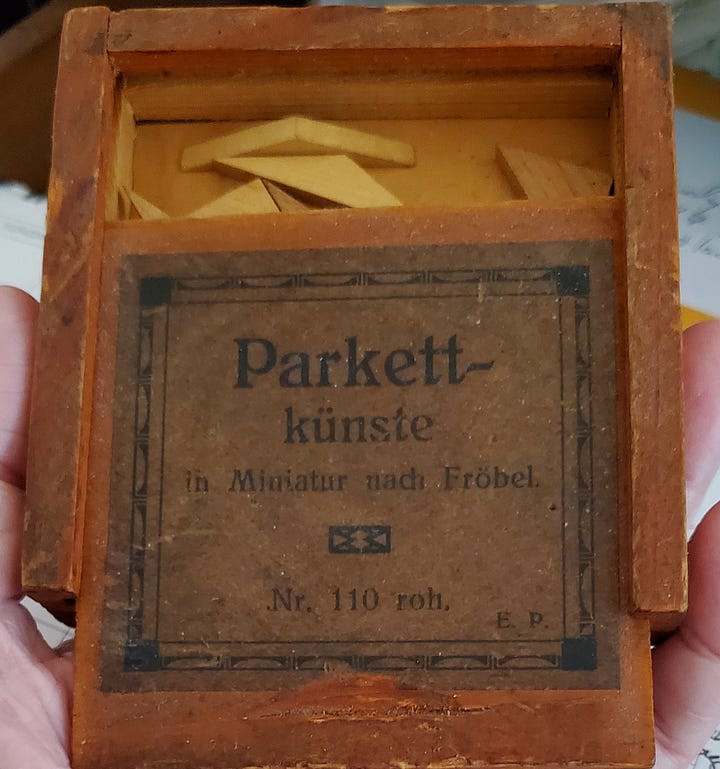 A small wooden box with triangular puzzle pieces inside, and a scribble of pencil outside.