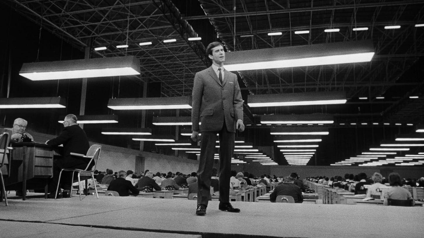 The Trial | Still features Anthony Perkins as Josef K on a desk, in an exaggerated bureaucratic setting.