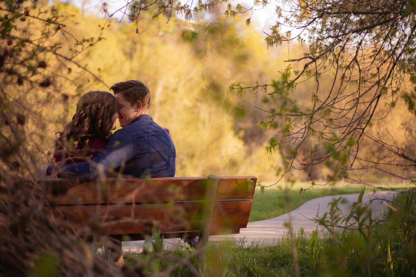 Woman and man sitting on a park bench, about to kiss