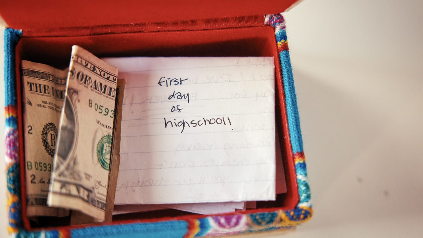 A box contains some dollar bills and a note that reads: "first day of high school!"