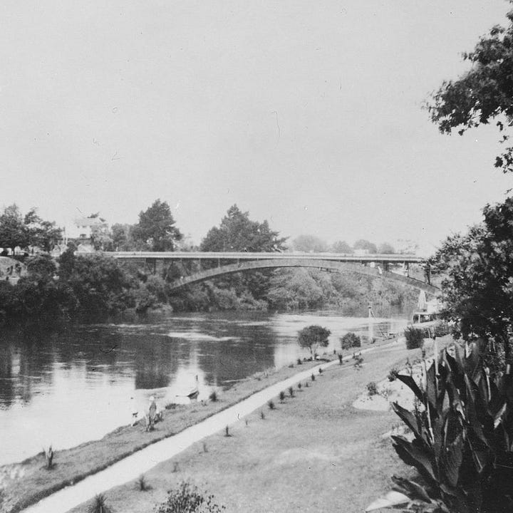 Left: A photograph taken from the west side of Victoria Bridge, looking east. You can see painted cyclelanes on both sides, a footpath on the north side of the bridge, and two lanes of traffic in the middle. Right: An old black and white photograph of the bridge, taken from the north west shores of the Waikato River. The bridge looks basically the same, but the landscaping under the bridge is very different.