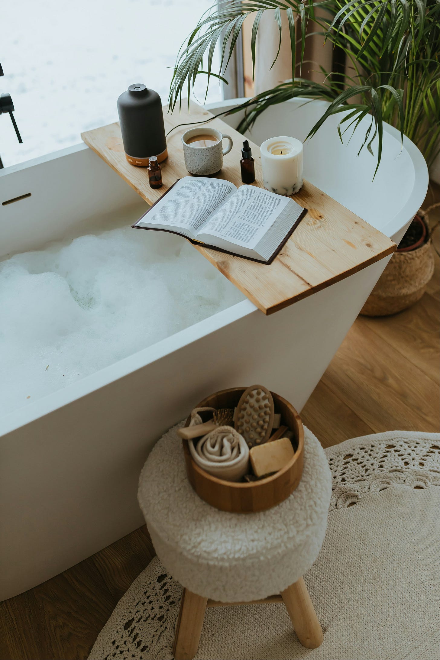 a self-care bubble bath with a book and cup of tea and diffuser next to it