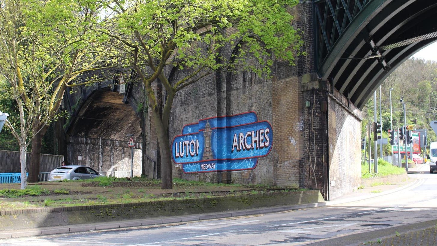 An arched railway bridge with a mural of the words 'Luton Arches' on the adjacent brick wall.