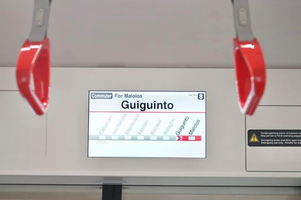 An interior shot of a PNR EM10000 Class, with a close up of its wayfinding screen running in demo mode. The top part of the screen says it's a commuter train bound for Malolos, with the current station at Guiguinto, and the viewer being located at the 8th train car. Below them is a train progress map