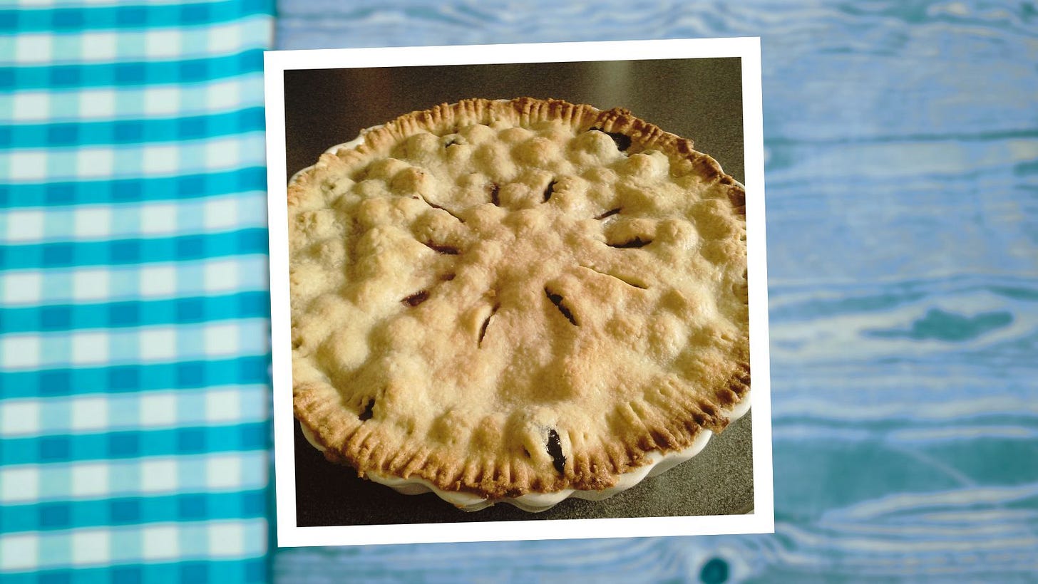 A Polaroid style photograph of a baked pie with fork-sealed crust sits on top of a turquoise tinted wood table with a turquoise checked napkin next to it
