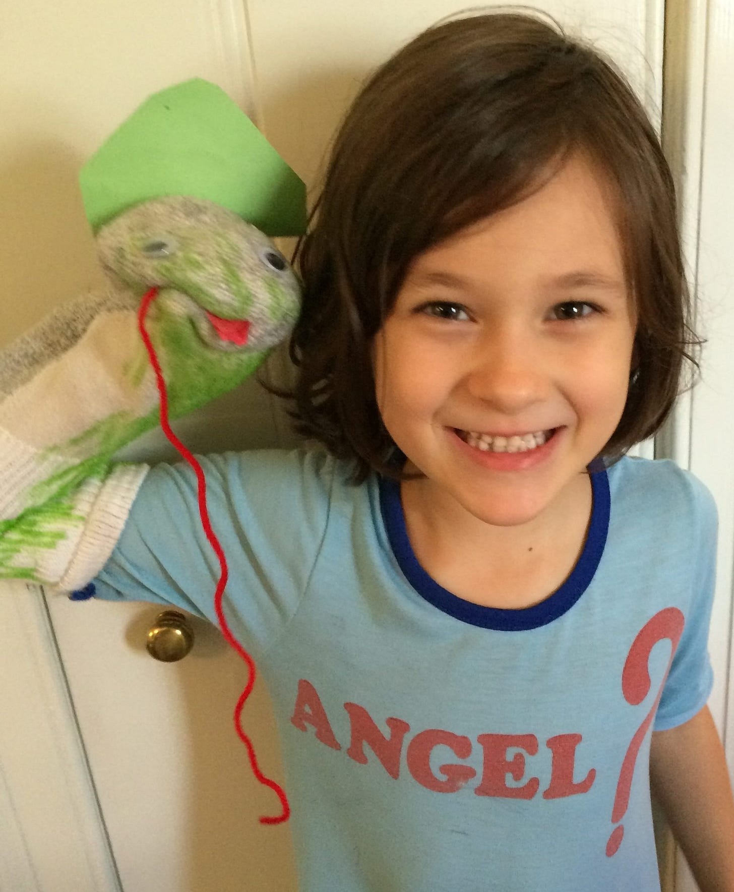 A little girl showcases her snake sock puppet. She's wearing a nightgown that says, "Angel?"