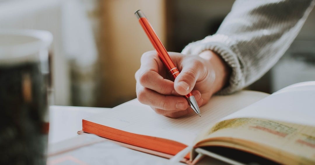 person holding on red pen while writing on book