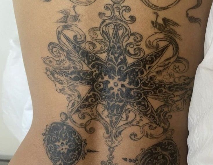 This may contain: a woman's back with an intricate tattoo design on her lower body and side