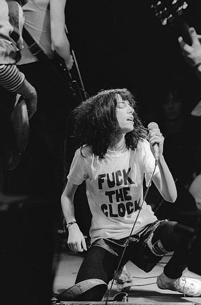 This may contain: a woman singing into a microphone while standing next to a man with long hair and wearing a t - shirt