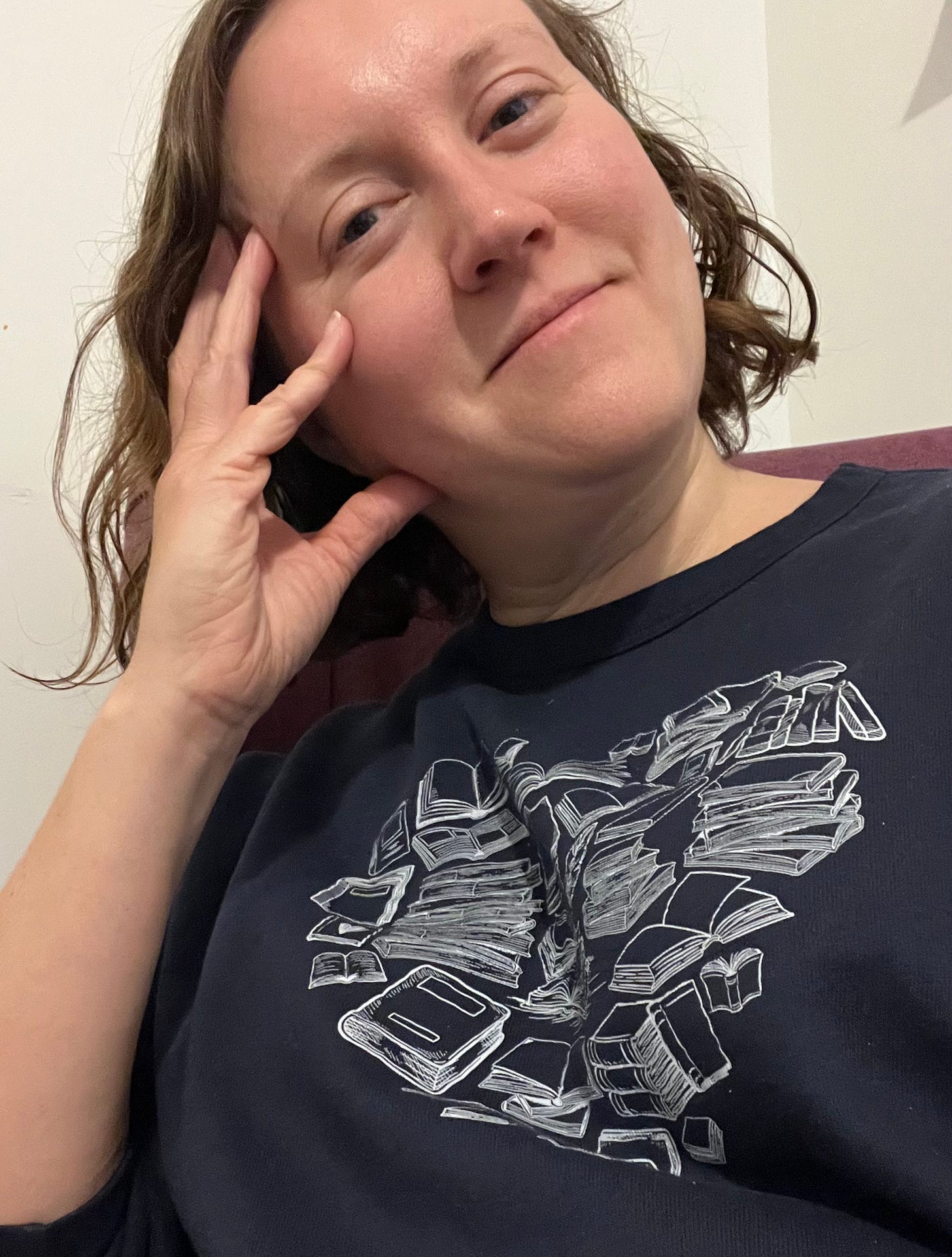 Kathryn is looking thoughtfully at the camera. She wears a navy blue sweatshirt with a design of books in a heart shape.