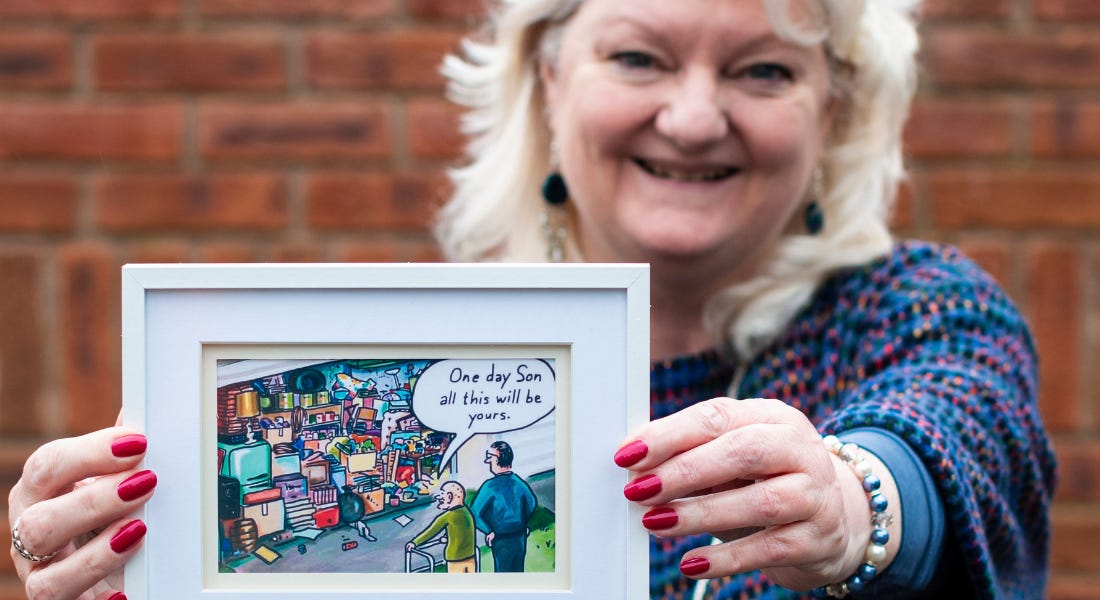 A picture of Pauline Webb holding a framed cartoon with two men and a garage A picture of Pauline Webb holding a framed cartoon with two men and a garage