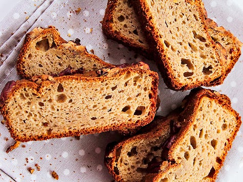 Homemade banana bread topped with pecans, shown whole and sliced to reveal a moist, tender crumb, styled with ripe bananas on a neutral linen background.