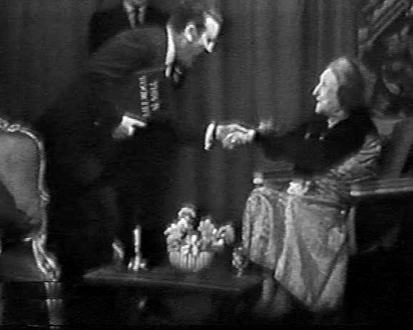 Grainy b/w image of a tv show. Eamonn Andrews is leaning over to take Edith Sitwell’s hand, and holding a just legible This Is Your Life book