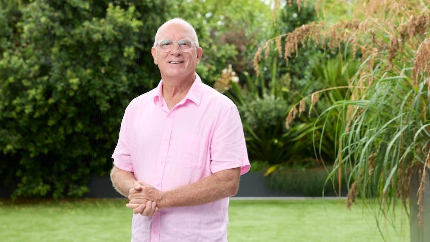 A smiling, older man in a garden.