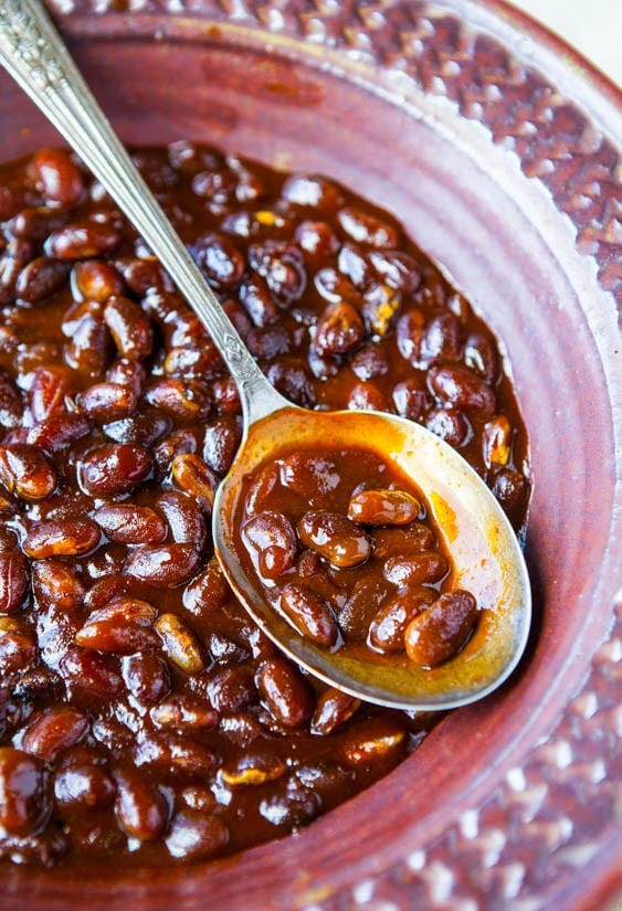 Bourbon Maple Slow Cooker Baked Beans (vegan, GF) - The best baked beans and the easiest! Set it & forget it! close up of bourbon baked beans in red dish with spoon