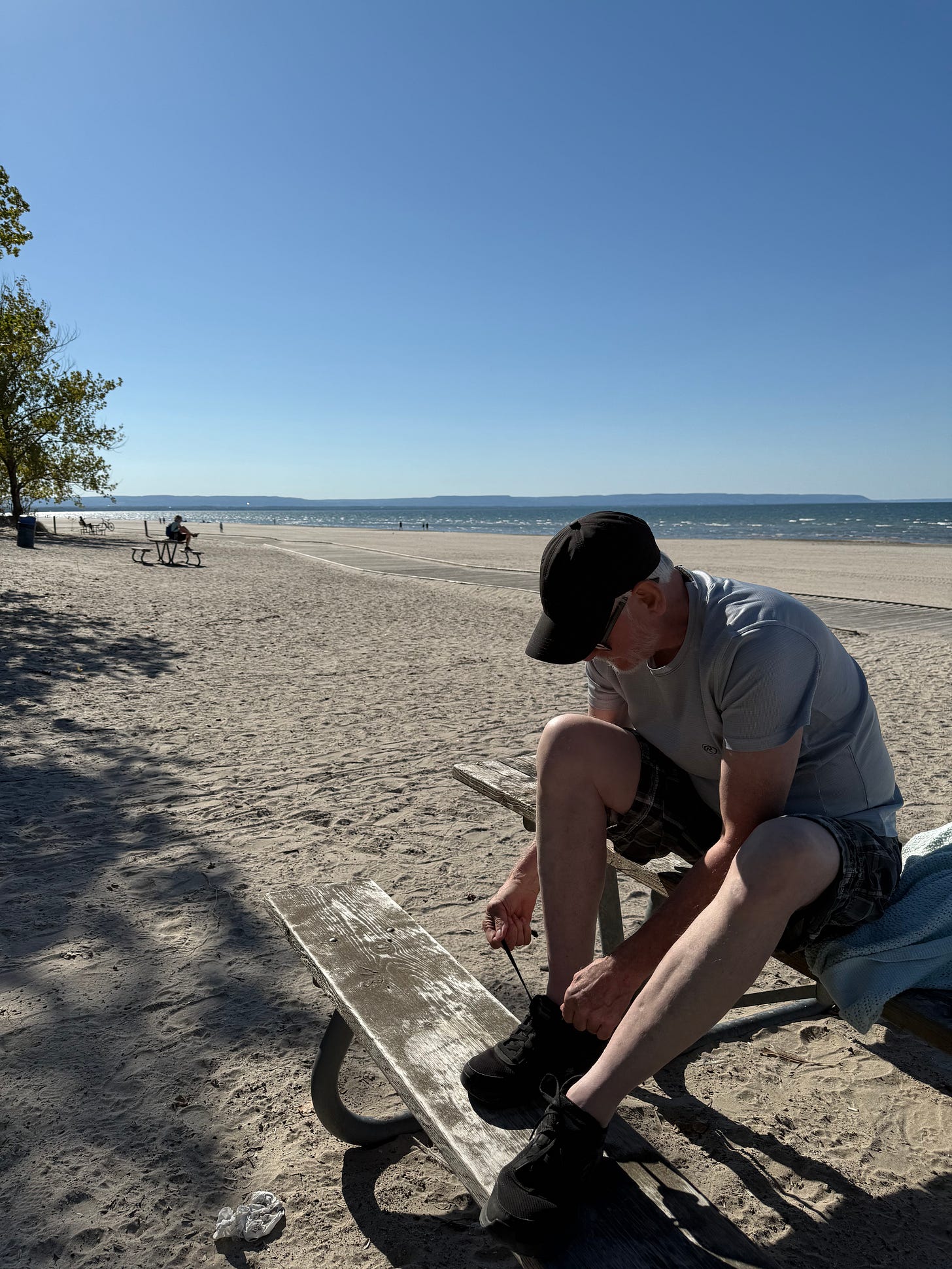 Man in shorts and cap sitting on a picnic bench at Wasaga Beach tying his shoes. Man in shorts and cap sitting on a picnic bench at Wasaga Beach tying his shoes.