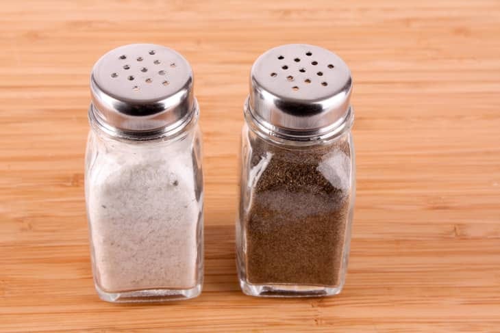 Salt and pepper shakers with metal lids on a wooden surface.