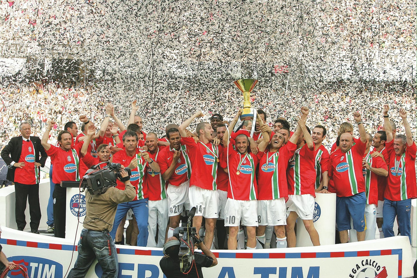 Juventus players celebrate winning the 2005 Serie A title, wearing special red shirts with a green and white stripe, as confetti rains down during the trophy presentation.