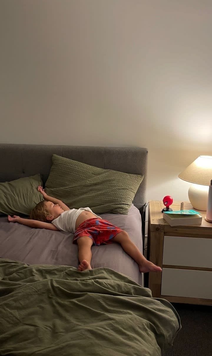 This may contain: a little boy laying on top of a bed next to a night stand and lamp
